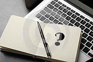 Notebook with question mark, pen and laptop on table, closeup