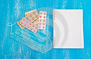 Notebook for recipes, protective medical mask, different pills on a blue wooden background