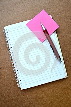 Notebook, red pen, pink note paper on wooden background.