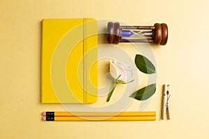 Notebook, sandglass, pencil, clip, rose on yellow gold background. Work and study place