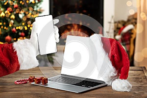 Notebook and smartphone with blank screen on rustic Christmas interior with fireplace. Christmas online shopping.