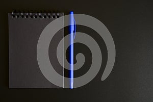 Notebook on a spring with black sheets and a blue pen on a black background. space for text.