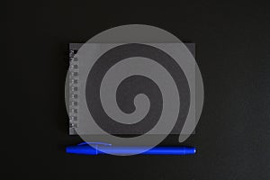 Notebook on a spring with black sheets and a blue pen on a black background. space for text.