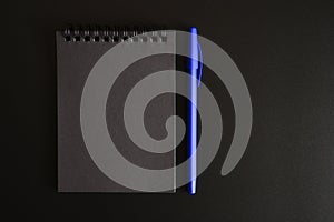 Notebook on a spring with black sheets and a blue pen on a black background. space for text.