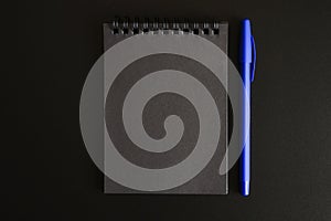Notebook on a spring with black sheets and a blue pen on a black background. space for text.