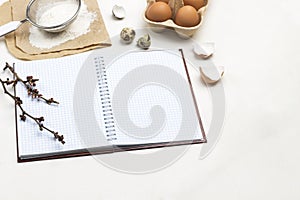 Notebook on springs. Two wooden spoons. Chicken eggs and chicken shells. Flour and sieve on paper