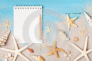 Notebook, starfishes and seashells on sand background top view. Planning summer holidays, trip, travel and vacation concept.