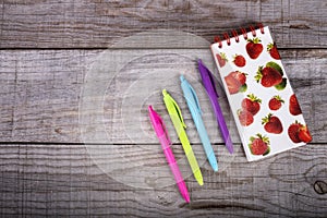 Notebook with strawberries and set of colored pens on wooden background