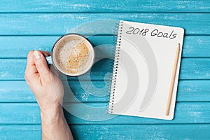 Notebook with text 2018 goals and cup of coffee on wooden desk top view. Planning and business concept. New year resolution.