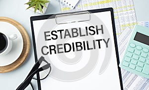 Notebook with text ESTABLISH CREDIBILITY sheet of white paper for notes, glasses in the white background