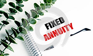 Notebook with text fixed annuity on white desk with pen and green plant decoration