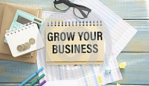 notebook, the text OF GROW YOUR BUSINESS, next to the pen, glasses and reports with graphs