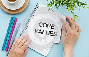 Notebook with text inside Core Values on table with coffee, laptop and some sheet of papers with charts