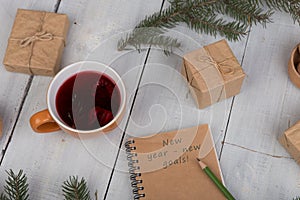 notebook with text "New year - new goals", pencil, gift boxes, nuts, fir branches and cup of tea photo