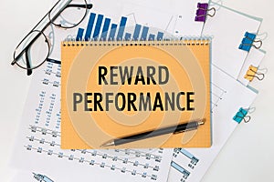 Notebook with text REWARD PERFORMANCE near office supplies