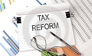 Notebook with text TAX REFORM on table with charts,pen and glasses