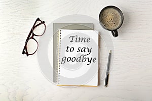 Notebook with text Time to say goodbye, office stationery and cup of coffee on white wooden table, flat lay