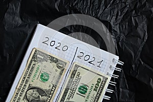 Notebook with two columns 2020 and 2021 a bundle of american dollars in a girl`s hand on a black background