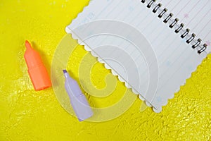 Notebook and two markers on a yellow embossed surface