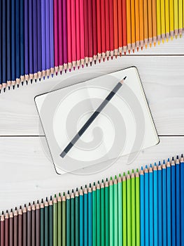 Notebook and two rows of colored pencils on wooden background