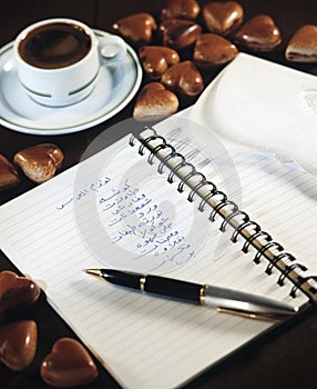 Notebook with wedding party shopping list beside a cup of coffee and chocolate hearts still life