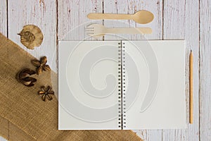 Notebook with wooden spoon and fork over the wooden table.