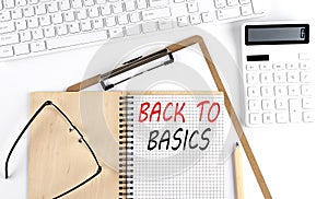Notebook with the word BACK TO BASICS with keyboard and calculator on the white background