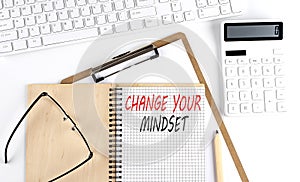 Notebook with the word CHANGE YOUR MINDSET with keyboard and calculator on the white background