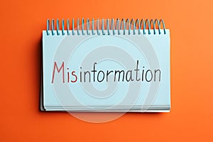 Notebook with word MISINFORMATION on orange background, top view