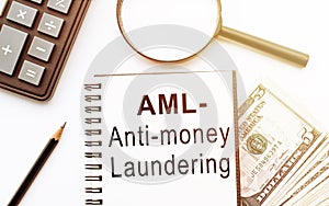 Notebook with words Anti-money laundering AML on table with calculator , magnifier, dollars and pencil