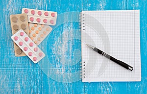 Notebook for writing recipes and different pills on a blue wooden background