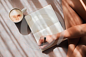 Notebook, writing and woman hands with coffee for ideas, inspiration and creativity on floor above in sunshine. Creative