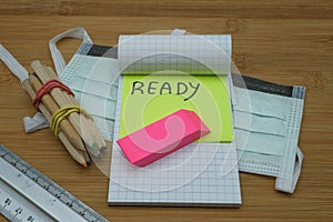 A notebook with written ready,a pink eraser some colored pencils, a ruler and a mask for the face