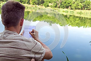 Notebook of a young man, a man close to the lake, painting landscape in Notepad. Summer Sunny day photo