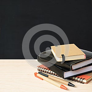 Notebooks and pens on wooden table with school black board