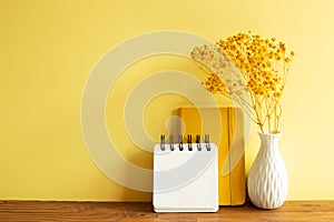 Notebooks and vase of baby`s breath flowers on wooden table. yellow wall background
