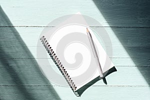 Notepad with blank sheet and pencil on turquoise blue wooden table in sunlight. Top view, flat lay, mockup