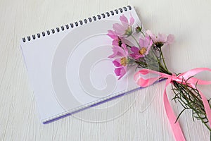 Notepad with a bouquet of delicate pink flowers, top view, space for text