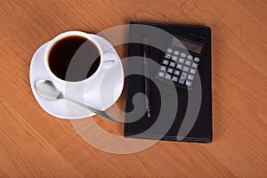 Notepad, calculator and cup of coffee on wood