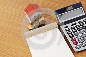 Notepad with Coins stack and paper house with calculator on wood