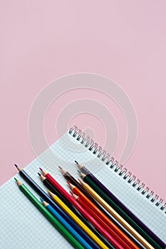 Notepad with color pencils on pink background with copy space.