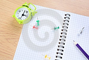 Notepad with colored pencil, clips and alarm clock on a table