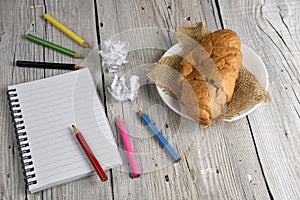 Notepad with colored pencils and croissant