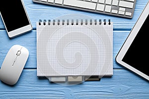 Notepad with copy space, smartphone, tablet and computer mouse and keyboard on blue table