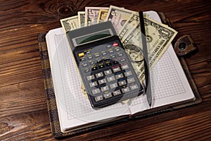 Notepad with dollars, pencil and calculator on wooden desk. Financial planning concept