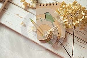 Notepad and dried flowers on a white wooden background.