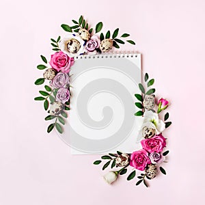 Notepad and floral frame in pastel colors. Happy easter concept. Roses, leaves and quail eggs around blank clean sheet