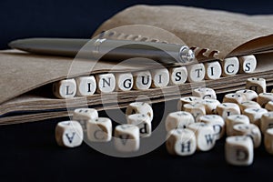 Notepad, fountain pen and the word linguistics made up of wooden cubes on a dark background. A concept for college liberal arts