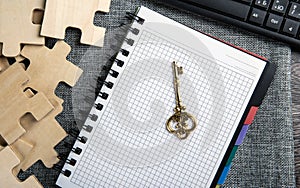 Notepad with a gold key symbol, pc keyboard and puzzle pieces