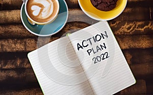 Notepad with the inscription ACTION PLAN 2022. A cup of coffee on a table in an ooffice or at a business lunch, concept image. photo